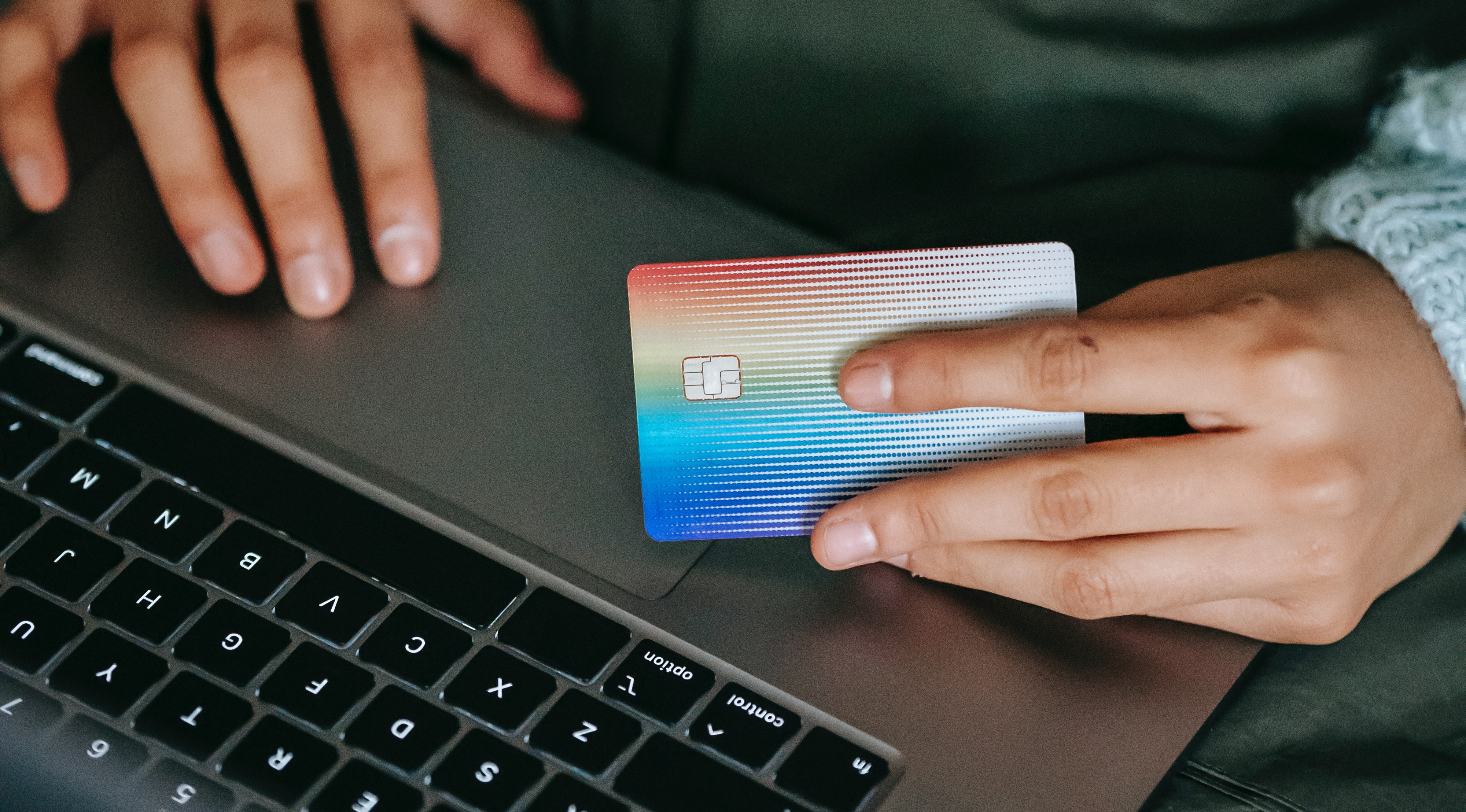 A man holds a credit card in his hand while scrolling on a laptop