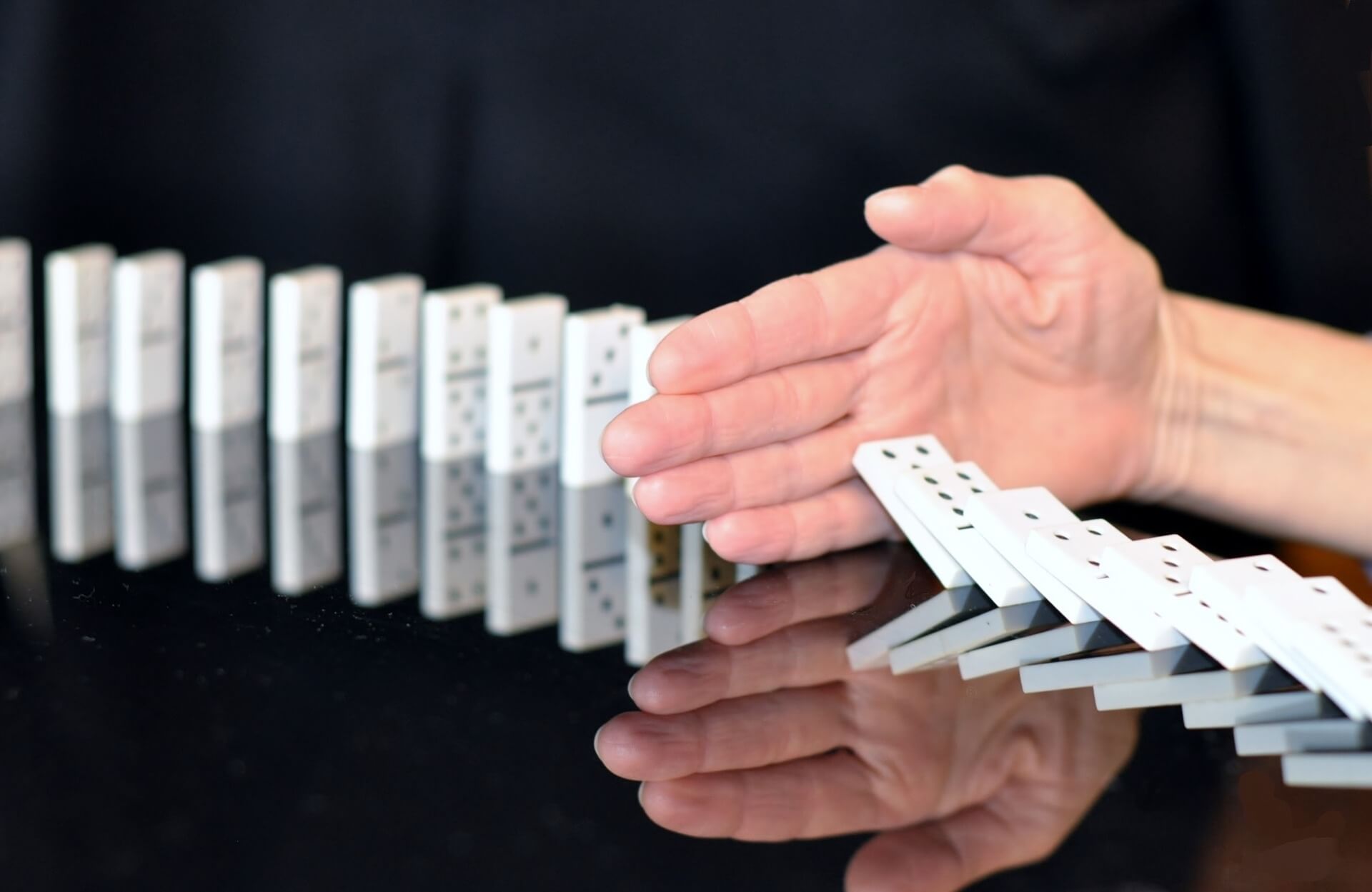 A hand stops a row of dominoes from falling